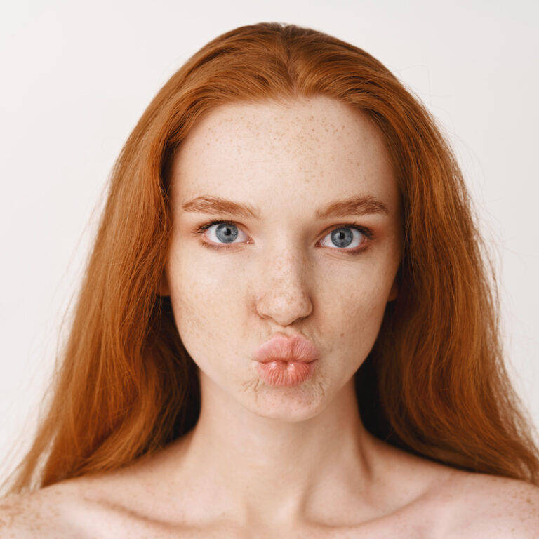 Close-up of beautiful young woman with long ginger hair. Redhead female with pale perfect skin, standing no makeup and pucker lips in kiss, looking with blue eyes at camera