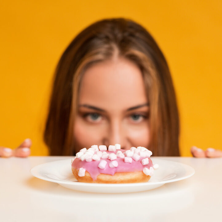 Hungry woman looking at donut with appetite, peeking out of table