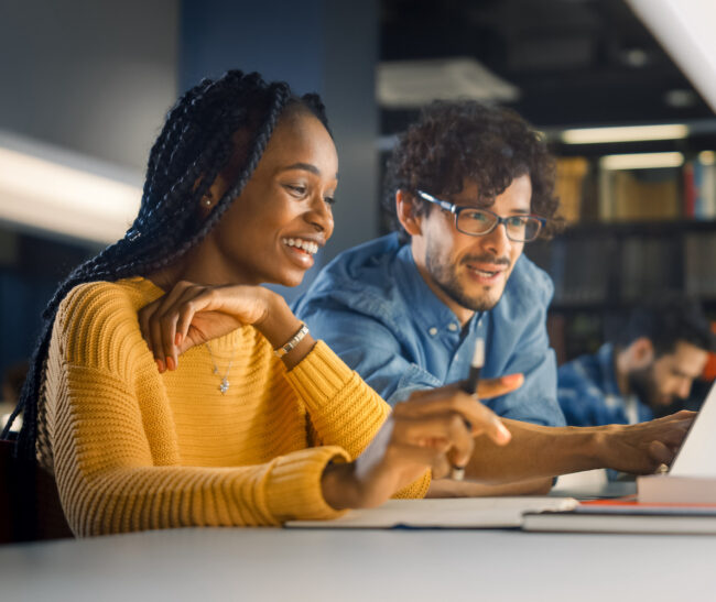 University Library: Gifted Black Girl uses Laptop, Smart Classmate Explains and Helps Her with Class Assignment. Happy Diverse Students Talking, Learning, Studying Together for Exams