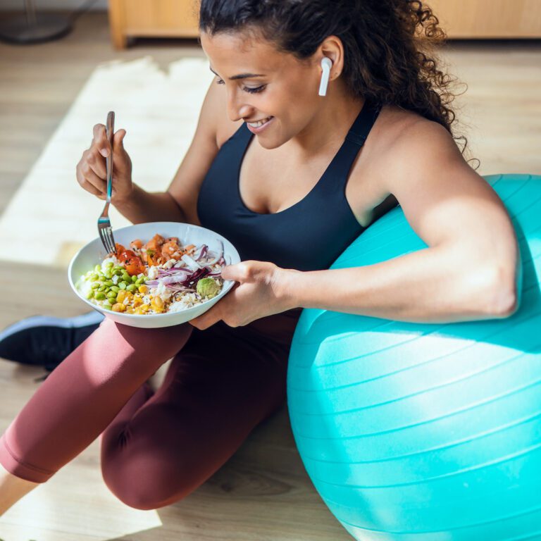 Sporty young woman eating healthy while listening to music sitting on the floor at home.
