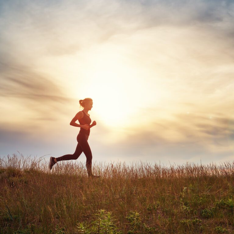 Young woman running on the field near seaside at sunset