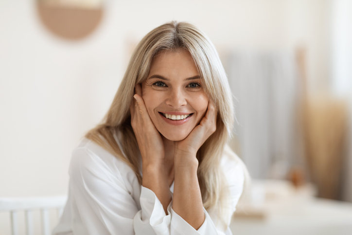 Beautiful middle aged woman smiling at camera, closeup portrait Beautiful blonde middle aged woman smiling at camera, touching her face, attractive lady doing morning face care routine, white bathroom interior, blurred background, closeup portrait, copy space