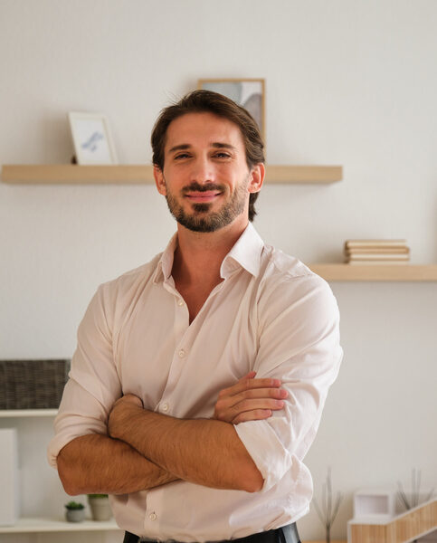 Young adult man standing, smiling at the camera in a modern office